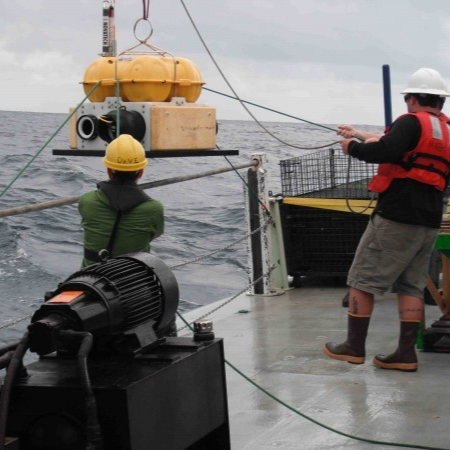 Crew on deck of research vessel lifting instruments out of the water.