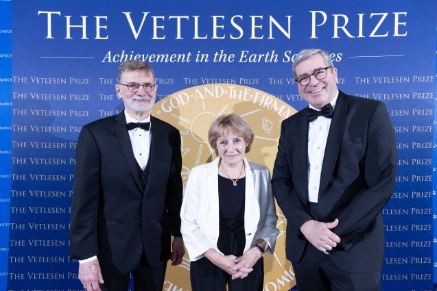 Two men and a woman in formal wear pose in front of a Vetlesen Prize backdrop