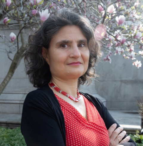 A woman in red and black stands in front of a tree