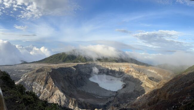 An expansive view of the Poas volcano crater beneath a blue sky.