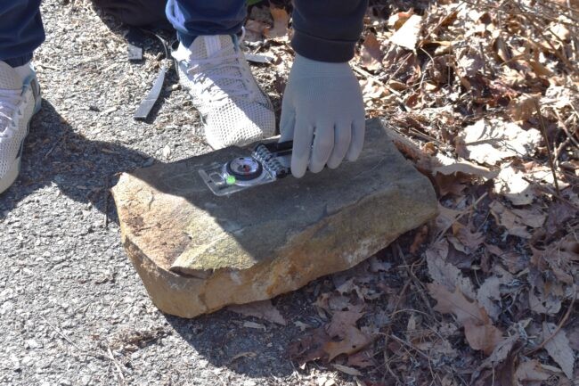Person puts a compass on a rock.