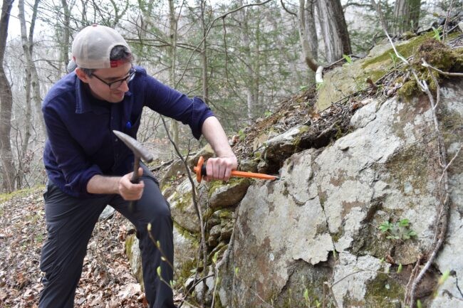 Man with hammer and chisel digging into boulder.