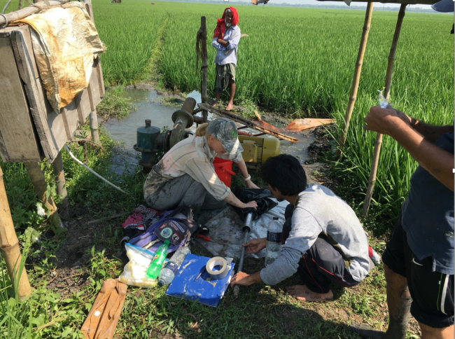 Liz Chamberlain collects a sample of mud from the abandoned Ganges River channel for optically stimulated luminescence dating. In the background, a pump delivers groundwater to irrigate rice which is often cultivated in relatively low elevation areas