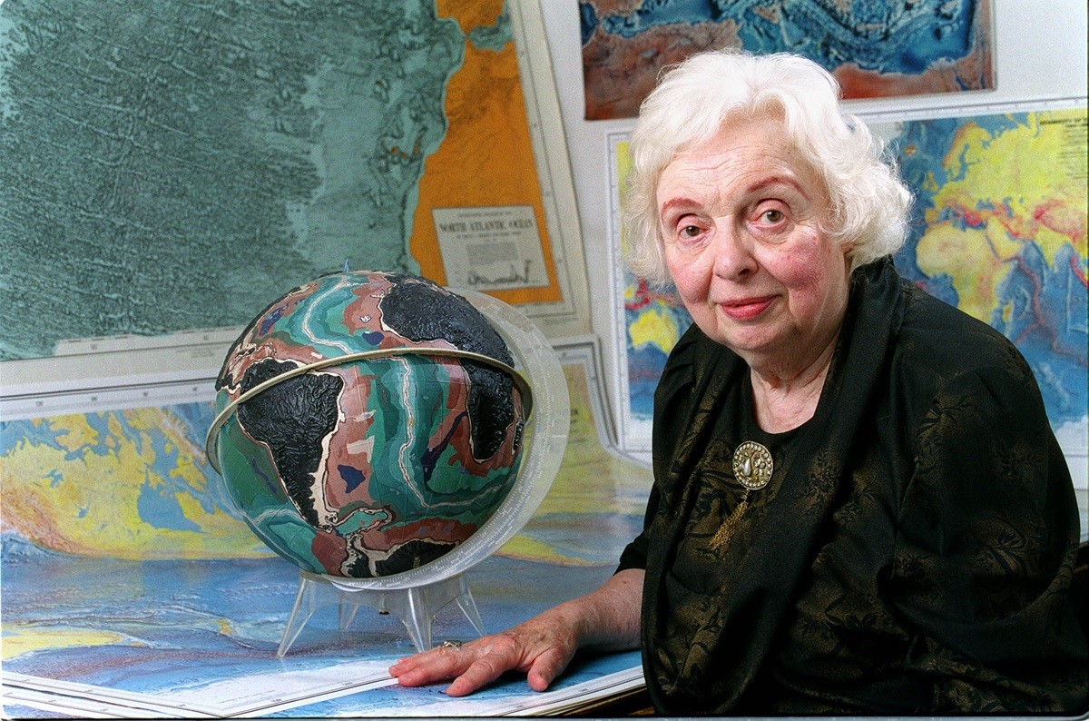 Marie Tharp in 2001 sitting in front of a bunch of maps and a model of the Earth