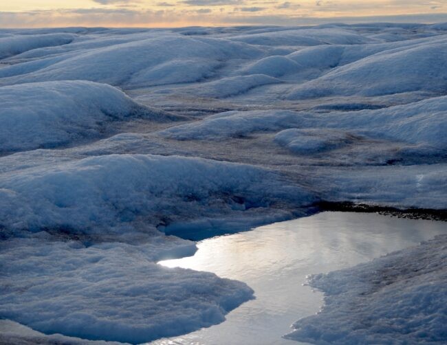 A melting pool of ice amid snowy peaks in Greenland