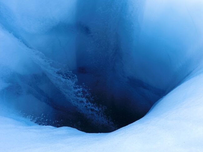 Meltwater flowing into a deep blue hole called a "moulin"