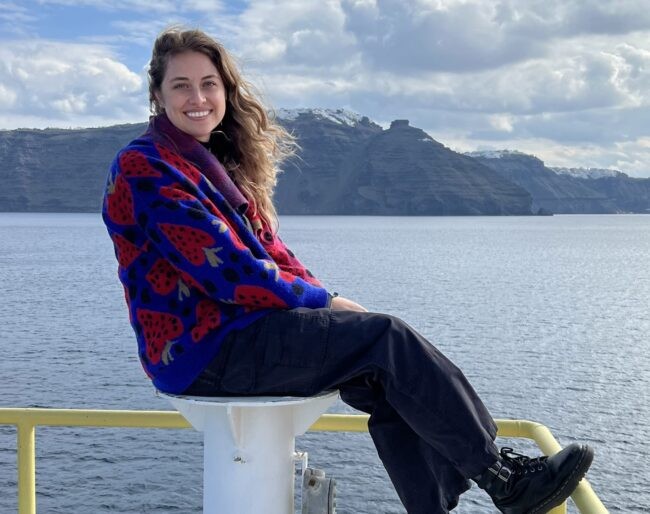 Lamont PhD candidate Ally Peccia, aboard a ship with a view of an island in the distance.
