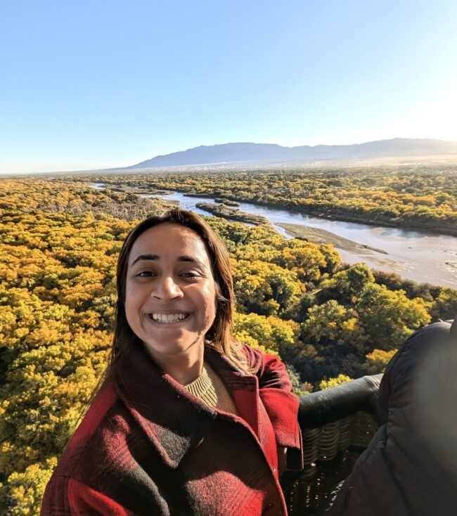 Woman takes selfie with aerial view of trees and water behind her