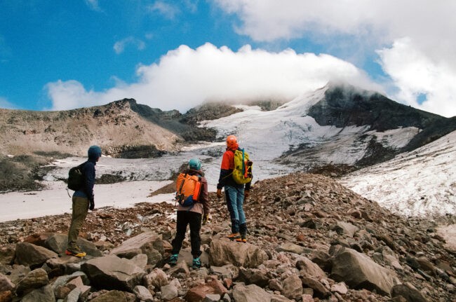 Three people in outdoor gear stand near glacier