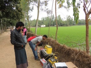 One of the Bangladeshi students checks the resistivity meter during the experiment while a local resident looks on.