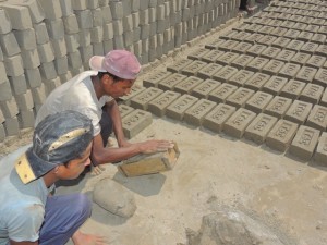 Tw of the workman shape the bricks using a mold.