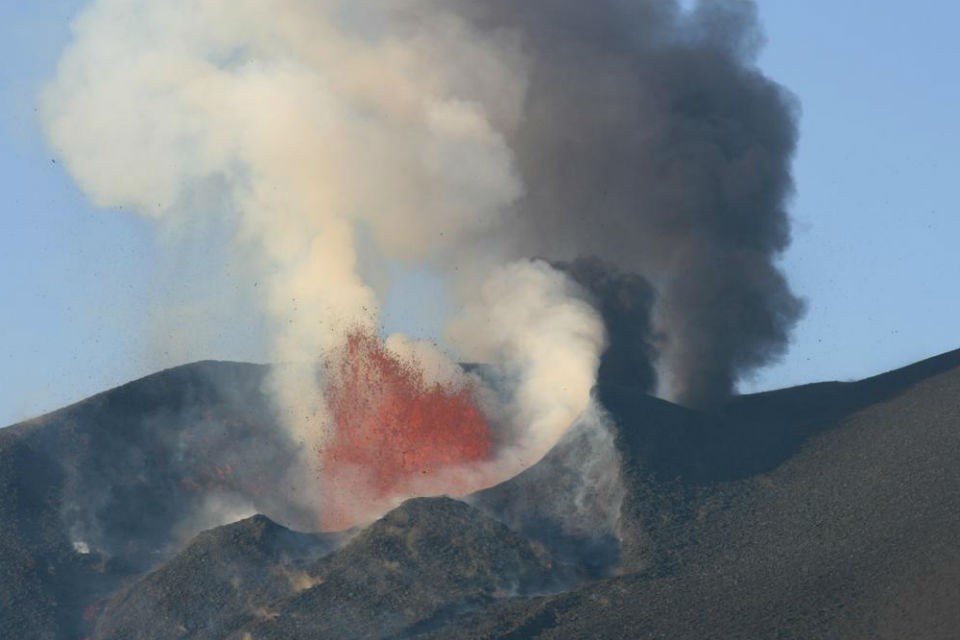 The volcano has erupted from several craters in many ways, from gentle effusion of lava to violent explosions of rocks and gases. Here, lava explodes from the main crater while columns of ash rise from a nearby vent. RR eruption 2 960