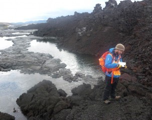 A graduate student takes notes about how the new lava flow (dark brown/black) is interacting with the  old flow (light gray) and  the river.