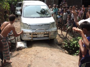 One of our cars drives over the makeshift road repair of a sandbag, bricks, wood and rebar while the entire village looks on.