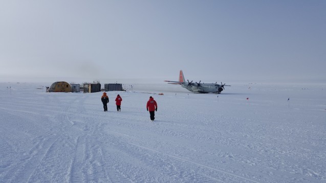 On the flight to the South Pole the LC130 hercules aircraft is the rear right parked at the edge of the skiway. The ice pod is on the far side the South Pole station. Team members Kirsty, Tej and Fabio are heading towards the South Pole passenger terminal waiting to reboard. (Photo N. Brady)