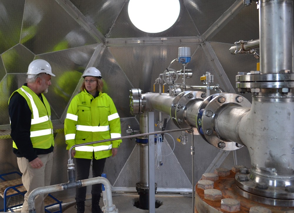  Martin Stute, a Lamont-Doherty Earth Observatory scientists who will be giving a live-streamed seminar about the CarbFix Project, talks with Edda Sif Arradotir of Reykjavik Energy in front of the piping system that pumps emissions back underground. Photo: Kevin Krajick