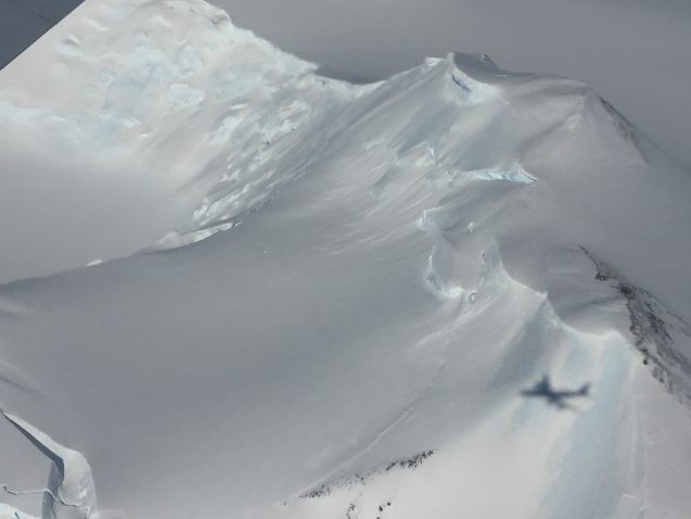 Mountains are buried under deep layers of ice. The shadow of the DC8 can be seen against the mountain. (Photo M. Turrin)
