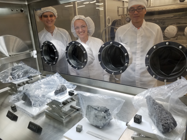 scientists in cleanroom gear looking at lunar rocks behind glass