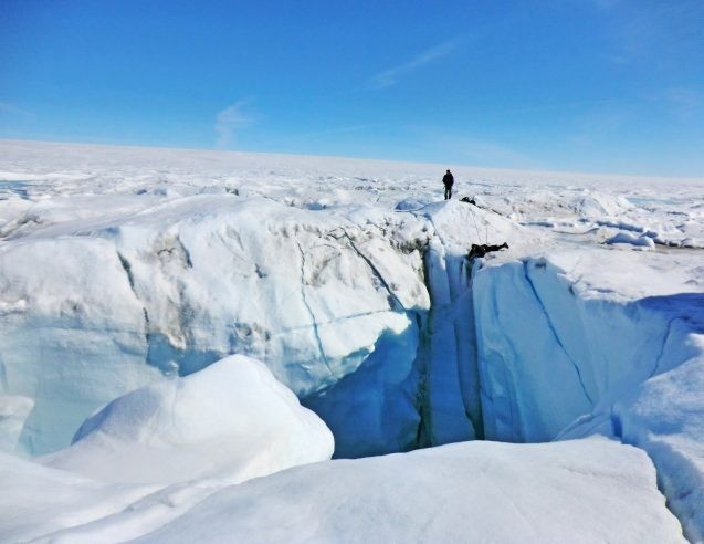 person standing near crevasse in greenland ice sheet