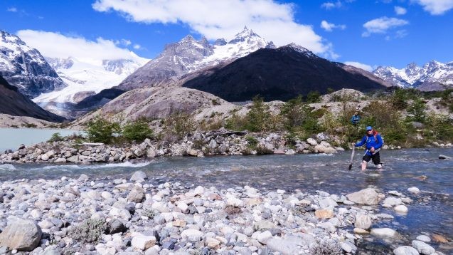 scientist crossing river with mountains in the background