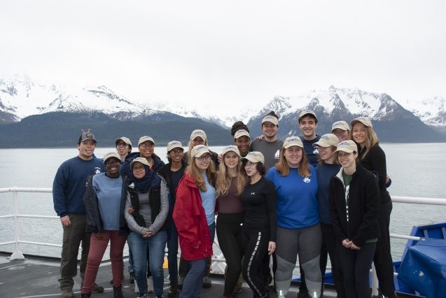 group photo aboard a ship with glaciers in the background