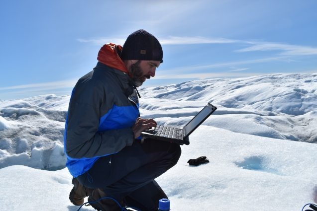 tedesco looking at laptop computer while sitting on ice sheet