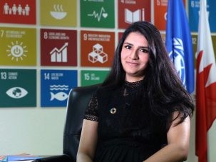 hadia sheerazi sits in front of a poster of the sustainable development goals
