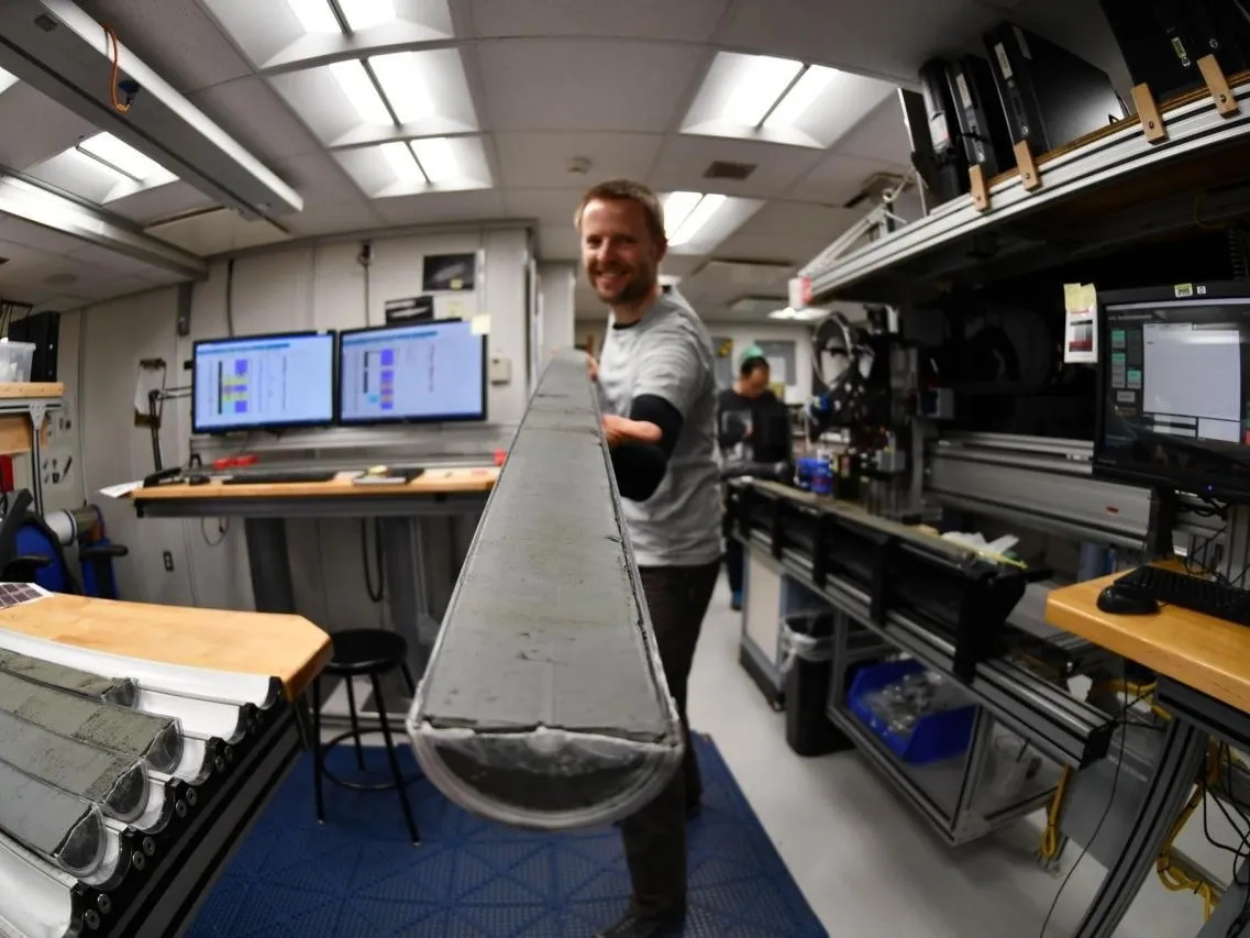 Aboard the drill ship JOIDES Resolution, a team member displays a sediment core. Credit: IODP