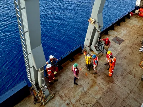 Science team and the Langseth crew moments before deploying an instrument. The team safely attaches the instrument to the A-frame which uses hydraulics to lift the instrument over the side of the ship and then release it to begin its descent to the seafloor. Credit: Brandon Shuck