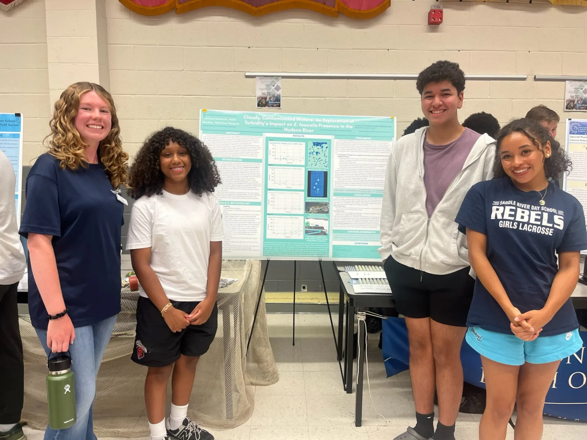 Next Gen Interns standing by research poster “Cloudy, Contaminated Waters.”