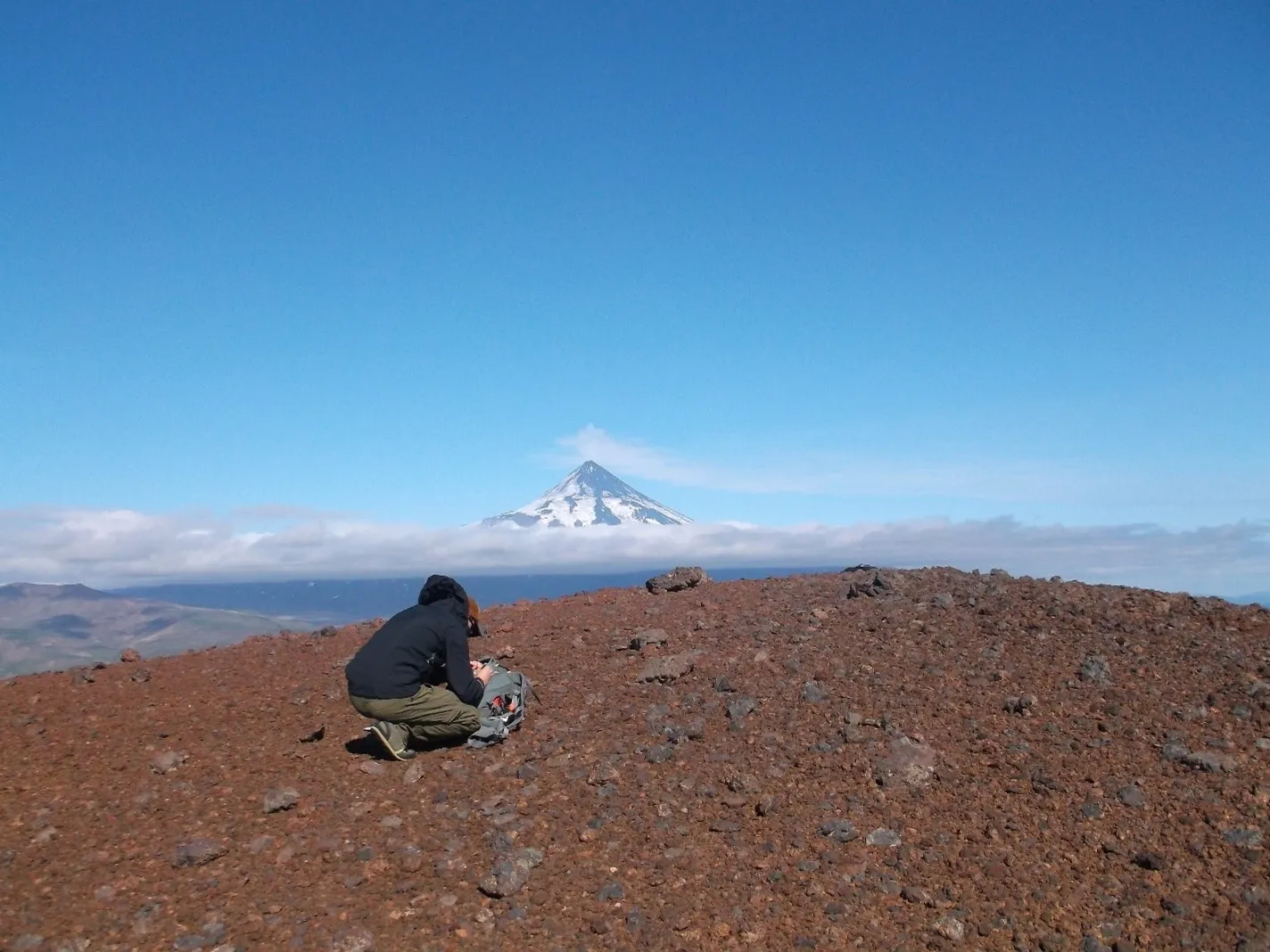 Water content controls the storage depth of magma under active volcanoes, says a new study. Here, lead author Daniel Rasmussen of Columbia University’s Lamont-Doherty Earth Observatory collects volcanic ash from the Aleutian Islands’ Fisher Caldera. Shishaldin Volcano looms in the distance. Credit: Diana Roman/Carnegie Institution for Science