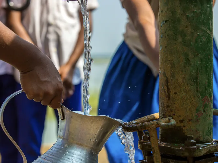 Stream of well water pouring into a metal pitcher. Credit: Lingkon Serao