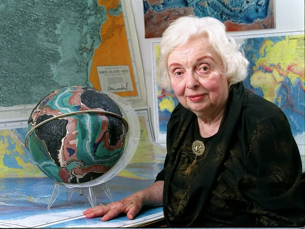 Marie Tharp in 2001 sitting in front of maps and a globe. Photo courtesy of Lamont-Doherty Earth Observatory and the estate of Marie Tharp.