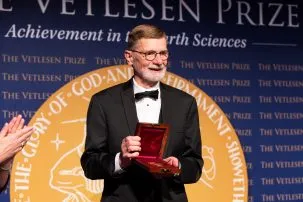 Man in tuxedo holds up a gold medal in a velvet lined box