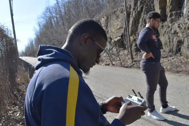 Man with console is piloting a drone. 