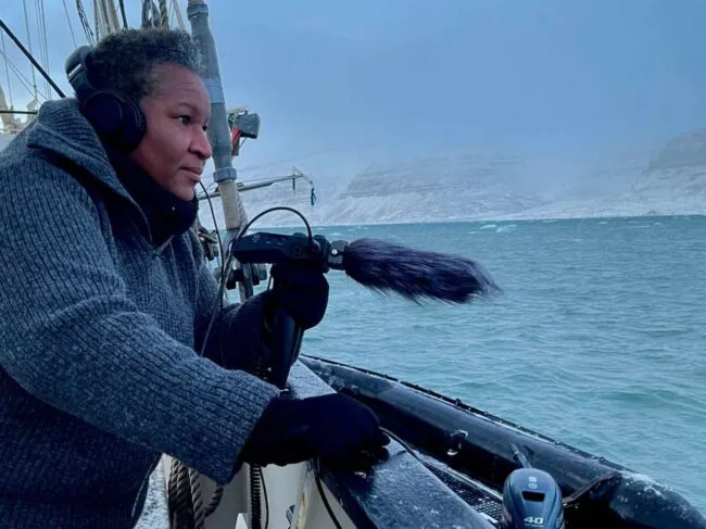 Woman recording sound over side of boat in cold terrain