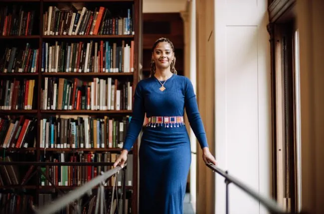 Douglass standing by a bookcase in a blue dress