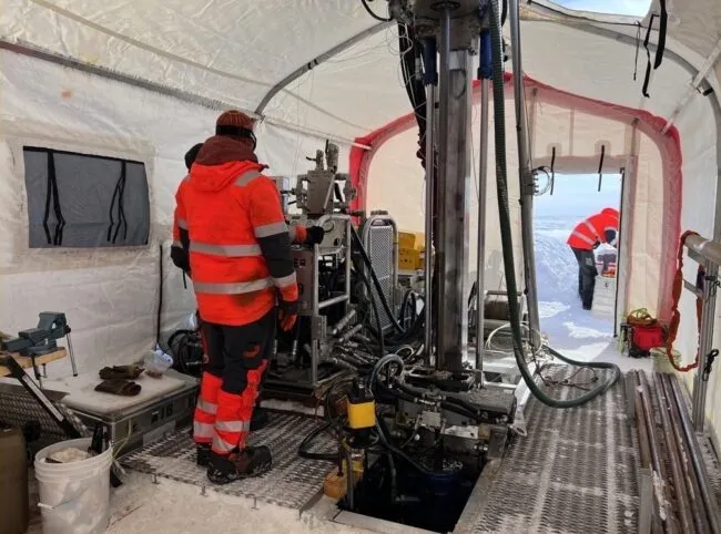 A large drill inside a tent, operated by someone in red gear.