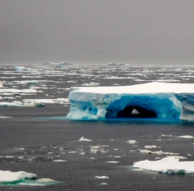Blue-tinted iceberg floating in a gray sea
