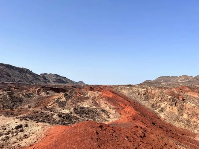 Layers of rock in different shades of red and brown, under a bright blue sky