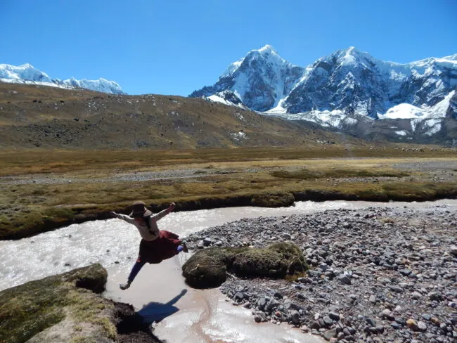 A young girl leaps over a river in the Peruvian Highlands