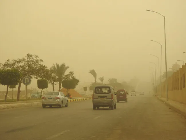 A blurry, yellowed view of cars on a highway, during a sandstorm. 