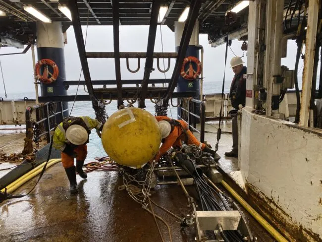 Deployment of seismic instrument aboard research ship with three crew members in hard hats