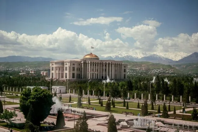 Large government building with a domed roof and fountains, set against mountains and a cloudy sky
