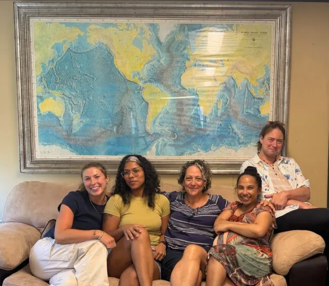 Vicki and her team sitting on a couch under a copy of the 1977 World Ocean map