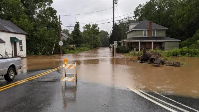 Flooded road with a house and sign blocking traffic