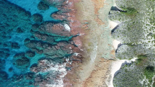 Aerial view of turquoise water, rocky reefs, and small sandy coves along a rugged coastline