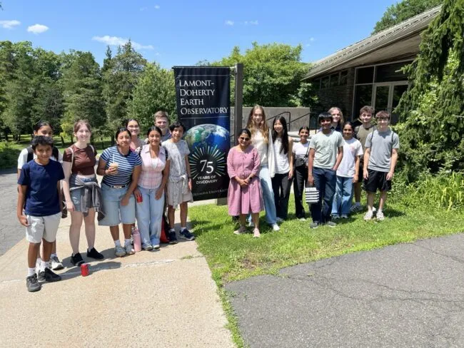 A group of students poses outside the Lamont-Doherty Earth Observatory beneath a sign celebrating 75 years of discovery