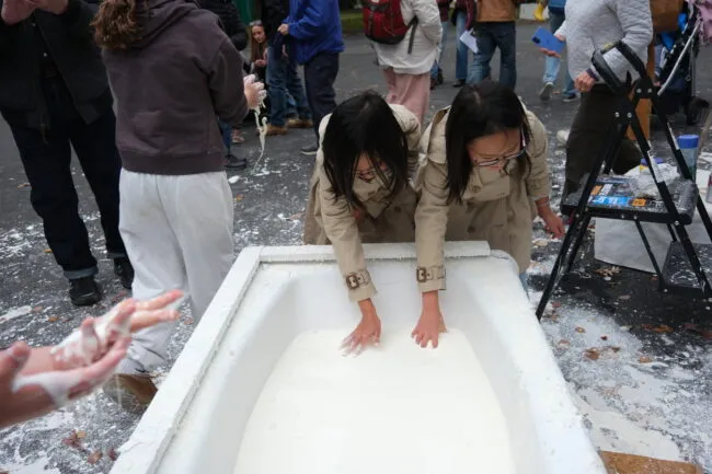People sticking their hands into a bathtub full of cornstarch and water for science learning