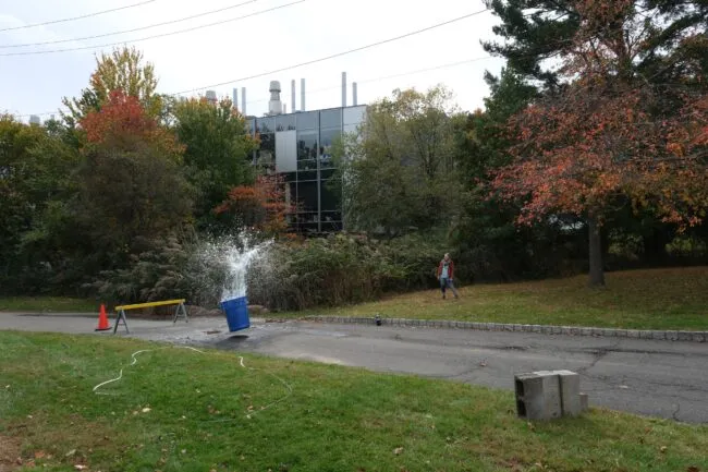 Campus with a trashcan volcano erupting in front of a modern building and a person standing nearby